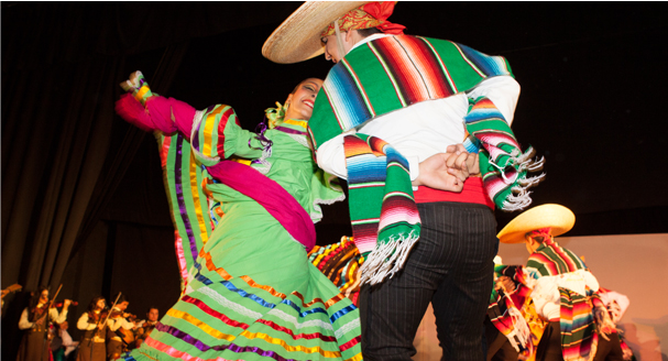 A man and woman in traditional Mexican costumes joyfully dancing together at a festive celebration.